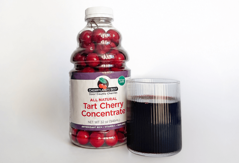 Glass of tart cherry concentrate next to a bottle of cherry concentrate filled with full cherries